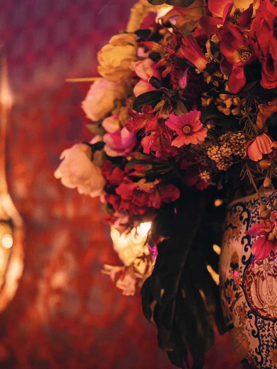 Boudoir wandlampen en bloemstuk tegen een rood damasten interieur